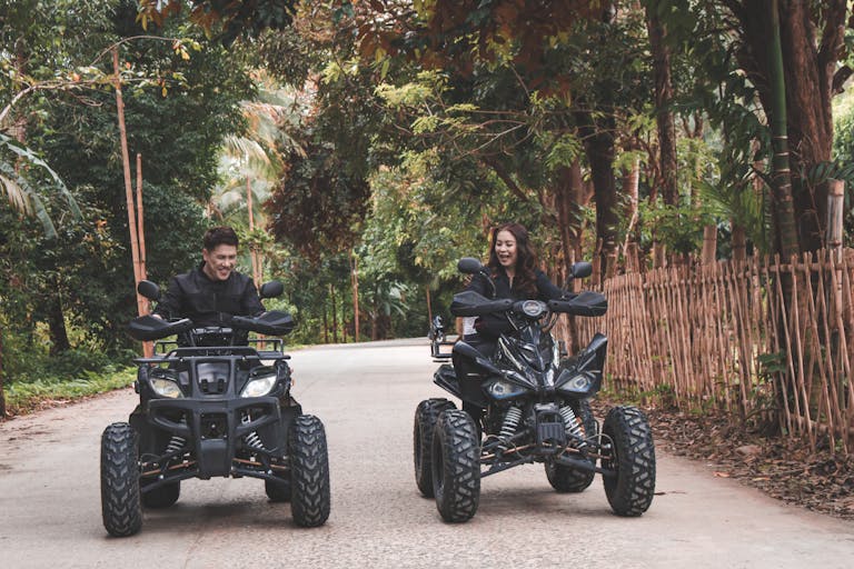 Couple riding quad bikes through lush countryside, enjoying a fun outdoor adventure.